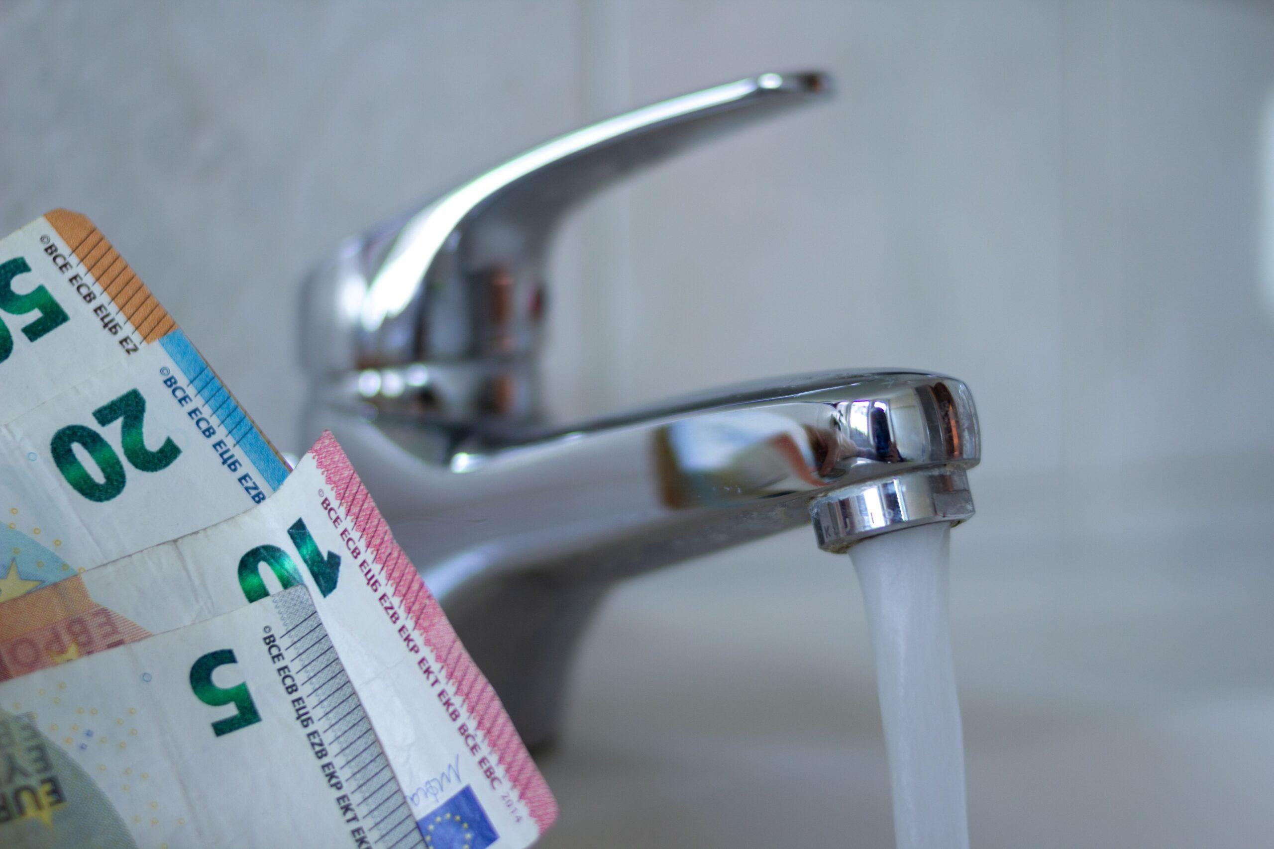 Ein Wasserhahn läuft und nebenan sind mehrere Geldscheine 