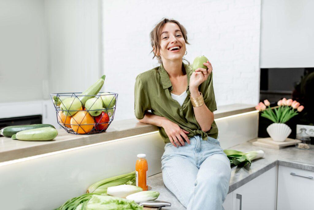 Porträt einer jungen und fröhlichen Frau mit gesunder Rohkost in der heimischen Küche. Konzept für Vegetarismus, Wohlbefinden und gesunde Lebensweise