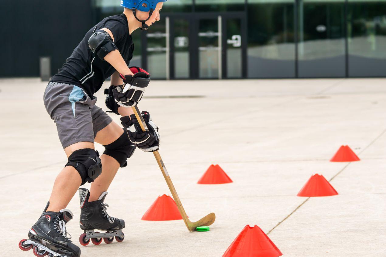Kind beim Inlinehockey-Training mit Helm und Schutzausruestung – Slalom zwischen Hütchen auf Betonplatz