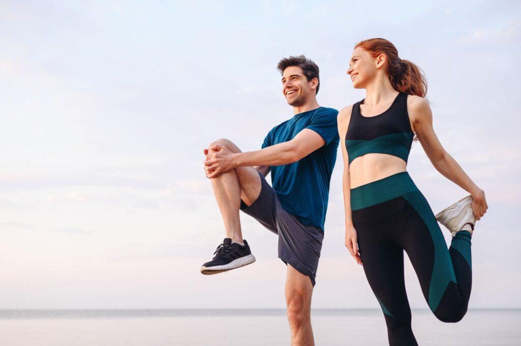 Sportliches Paar dehnt sich nach dem Training am Strand – Symbolbild fuer Praevention durch gezielte Nachsorge laut Sportorthopaede Koeln.