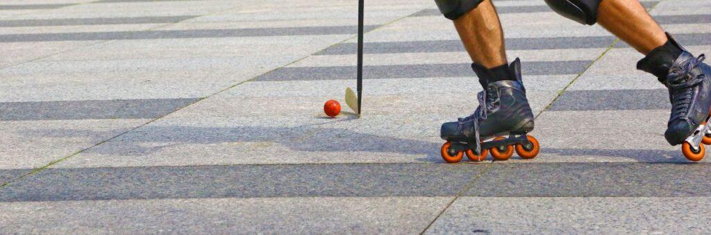 Inlinehockey-Spieler faehrt mit Ball auf Asphaltfläche – dynamische Szene beim urbanen Training