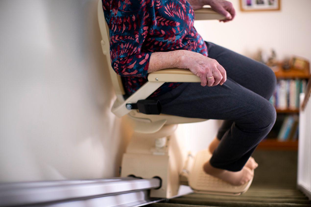 Seniorin sitzt auf einem modernen Treppe Lift im Hausflur zur besseren Mobilitaet