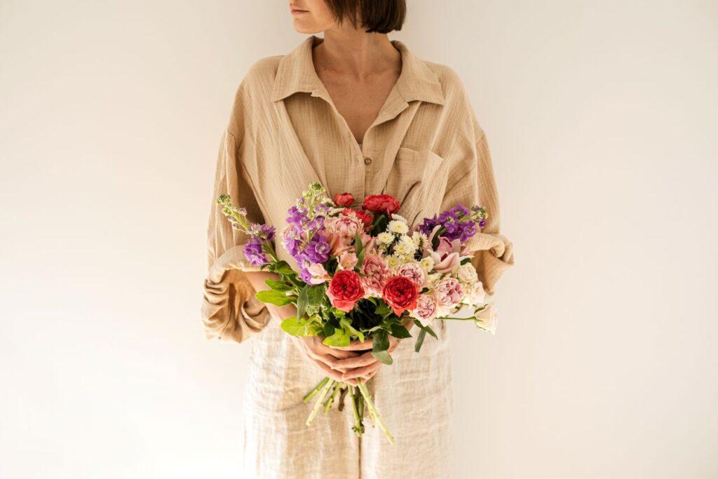 Musselin Kleidung in Beige getragen von Frau mit Blumenstrauss vor hellem Hintergrund