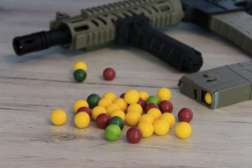 Nahaufnahme von Paintball Markierer mit Magfed Magazin und bunten Paintballs auf Holzboden, Symbol fuer Technik und Ausruestung
