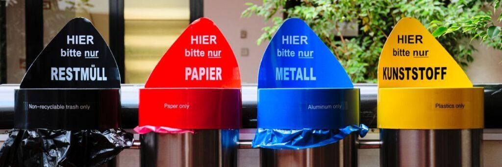 Aufkleber fuer Muelltrennung auf bunten Abfallbehaeltern fuer Papier, Metall, Kunststoff und Restmuell in Innenraeumen