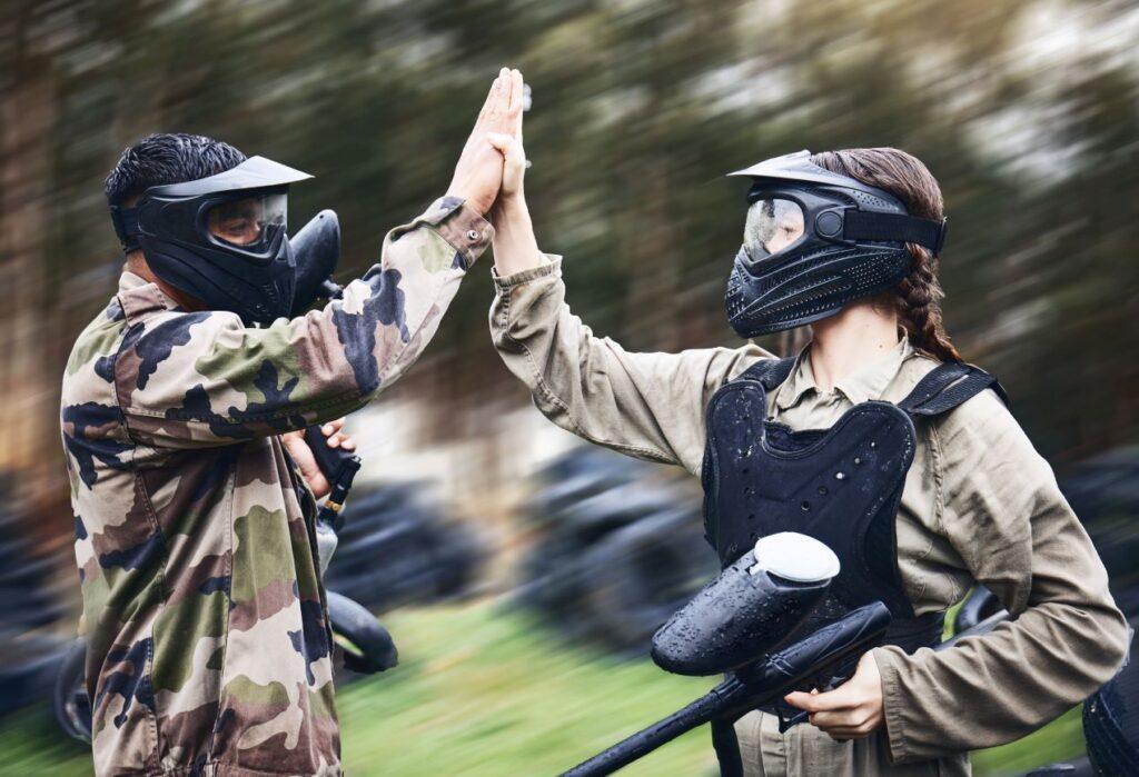 emf100 paintball spieler geben sich high five nach match im wald mit taktischer ausruestung und masken