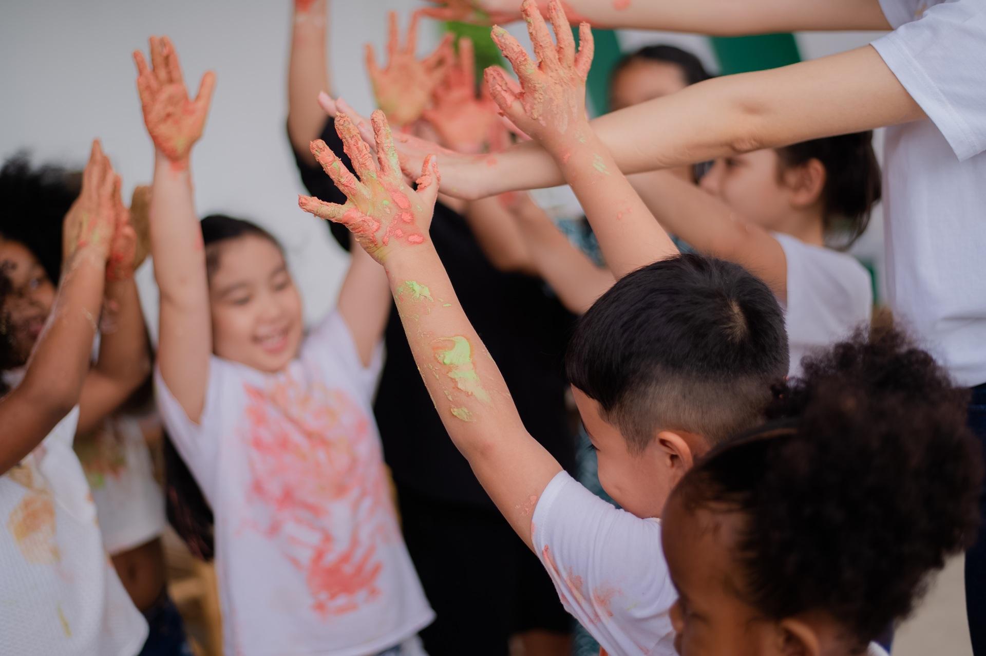 Kinder mit Farbresten an Händen heben Arme hoch | Grundschule Berlin